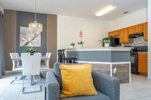 A modern kitchen with wooden cabinets, a central island, and a dining area with a white table and chairs. - 4 Bedrooms Close to Disney (Kissimmee)