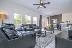 A modern living room with a leather sofa, a round coffee table, and a dining area with a chair and a table. - 4 Bedrooms Close to Disney (Kissimmee)