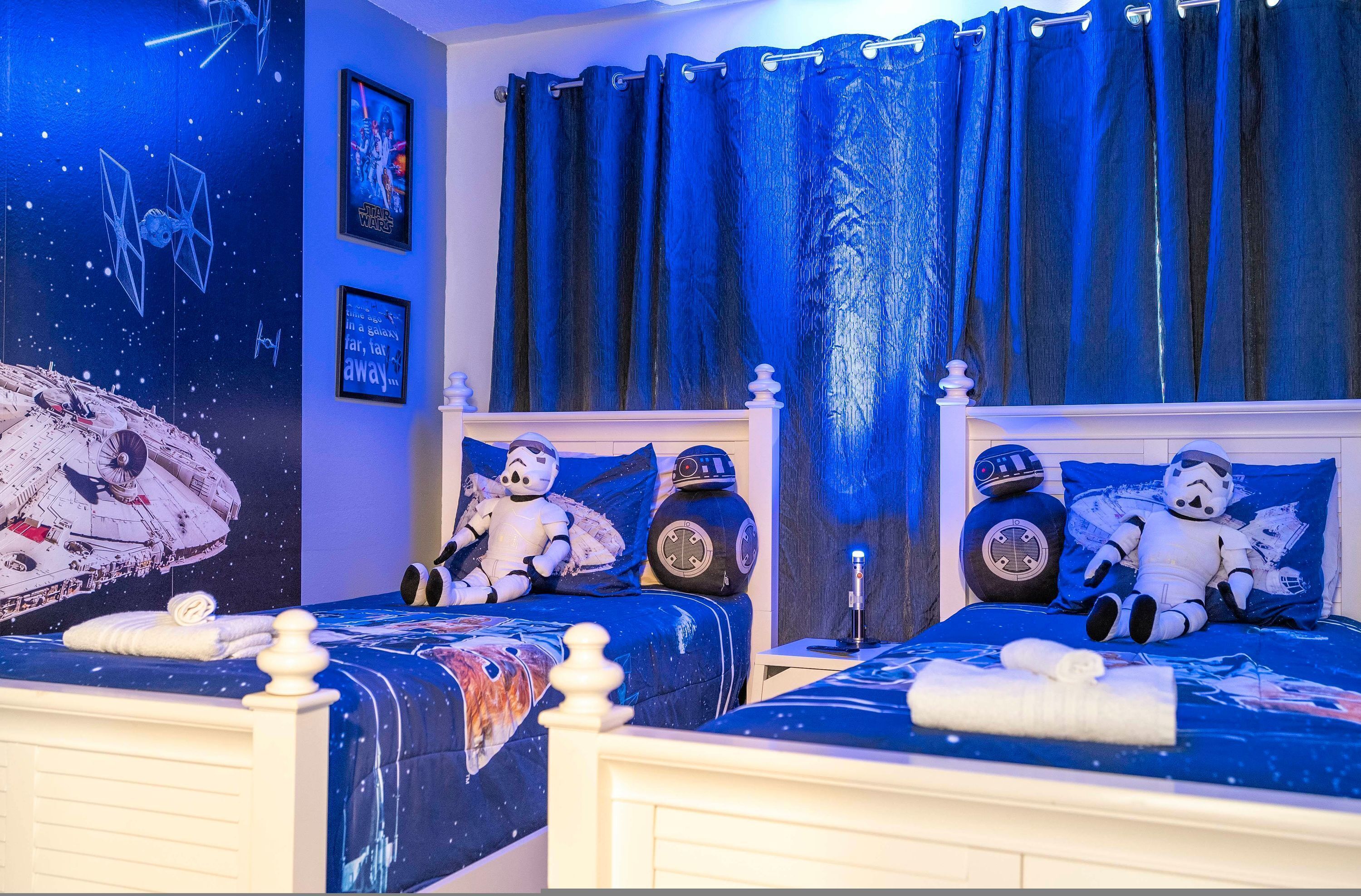 Ein Schlafzimmer mit zwei Betten, eingerichtet im Stil von Star Wars, inklusive Wandgemälde und Kissen, sowie ein Nachttisch mit Lampe.