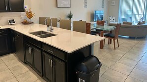 A modern kitchen with a central island, black cabinets, and a dining area with a glass table and chairs. - Fabulous 3 Bedroom With Game Room (Davenport)