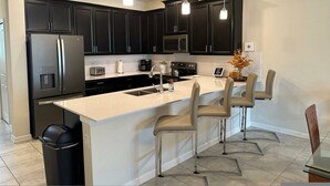 A modern kitchen with dark cabinets, a white island with bar stools, stainless steel appliances, and pendant lighting. - Fabulous 3 Bedroom With Game Room (Davenport)