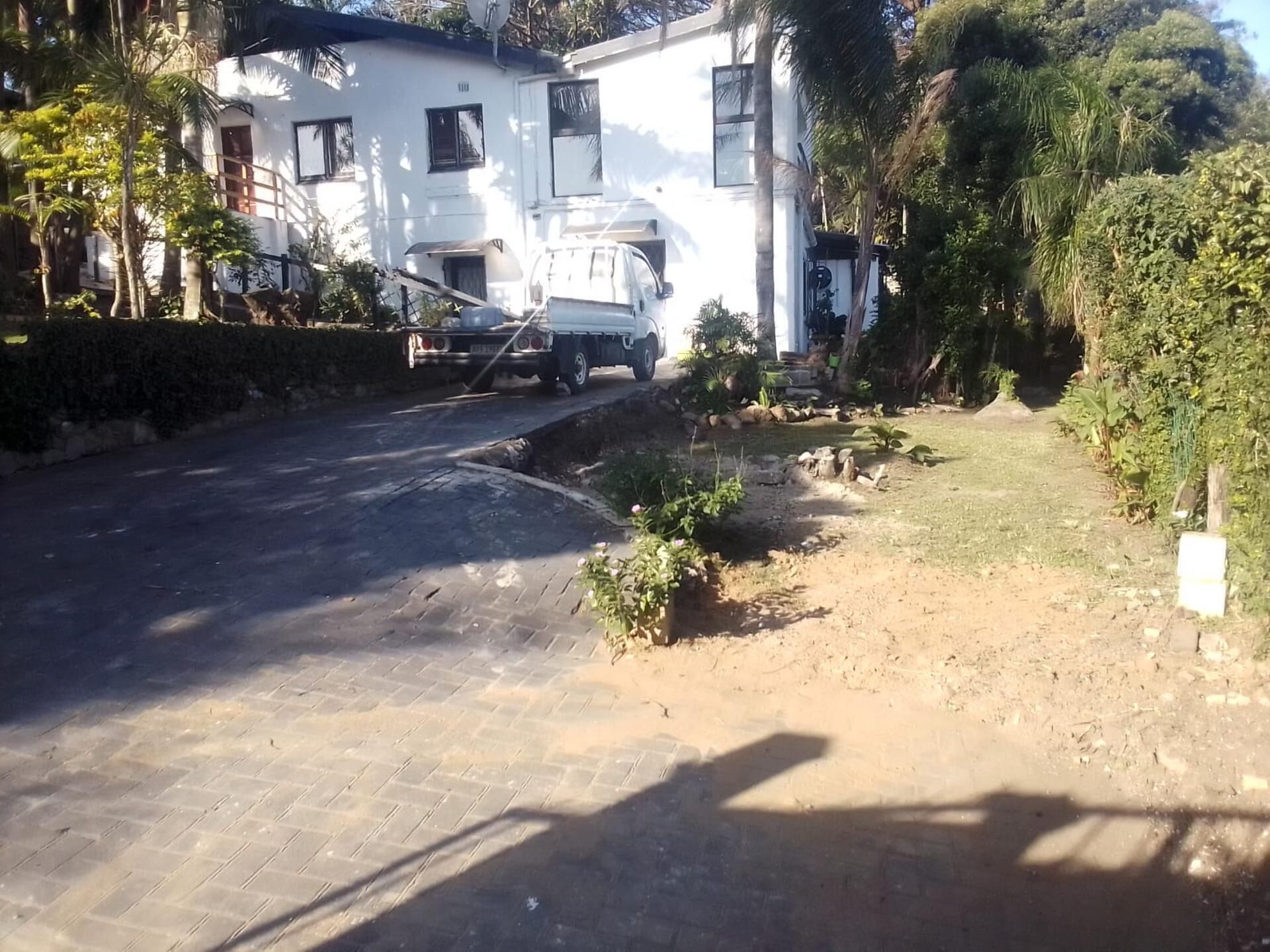 A residential driveway leading to a white house with a satellite dish, surrounded by greenery.