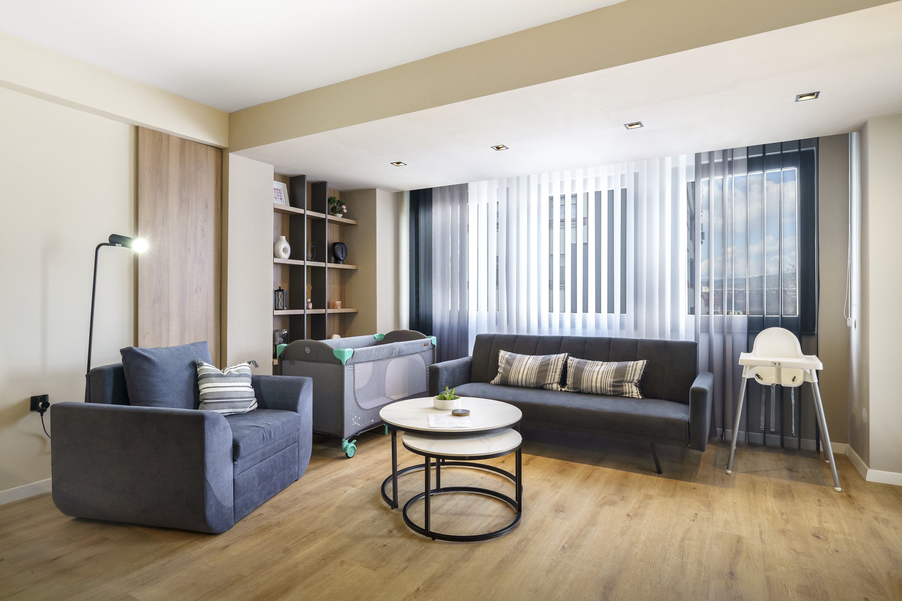 A modern living room with a grey sofa, a small round table, and a bookshelf.