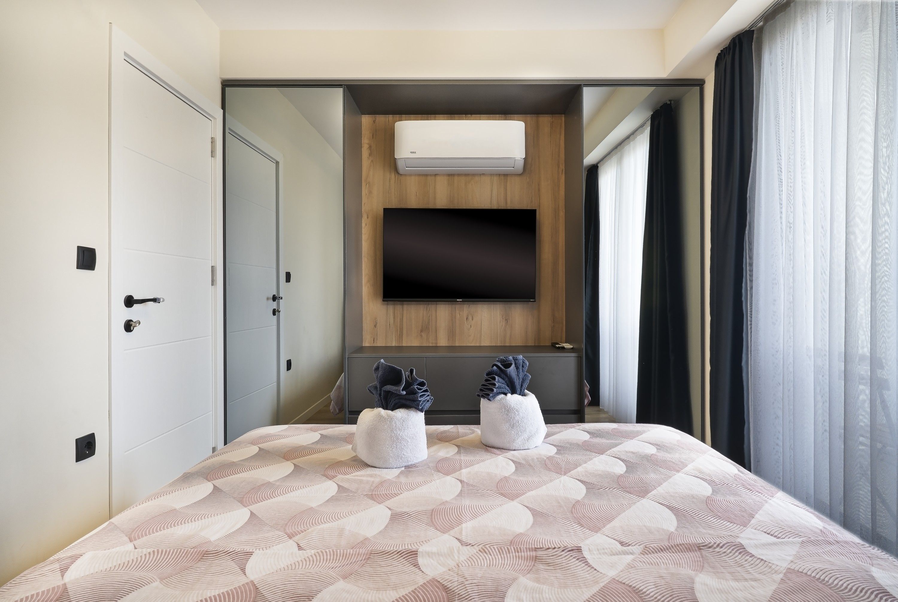 A hotel room with a bed, a TV mounted on the wall, and a window with curtains.