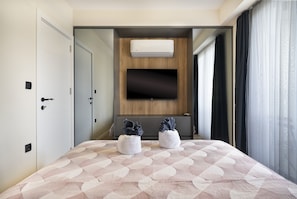 A hotel room with a bed, a TV mounted on the wall, and a window with curtains.