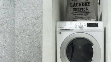 A front-loading washing machine with a control panel and a bag of laundry service on top.