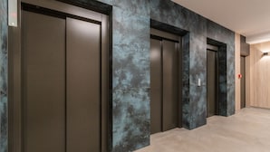 A corridor with three elevators and a wooden door at the end. - Letnica - Botanika by Grand Apartments (Gdansk)