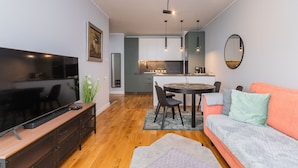 A modern living room with a flat-screen TV, wooden flooring, a sofa, and a dining area with a table and chairs. - Letnica - Botanika by Grand Apartments (Gdansk)