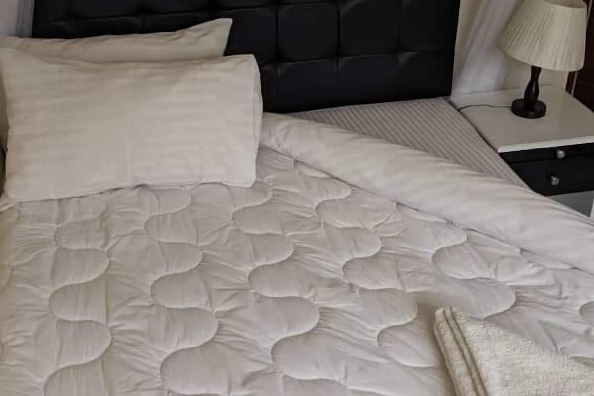 A neatly made bed with a white quilt, a black headboard, and a bedside table with a lamp.