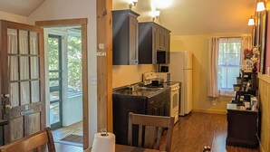Comedor con mesa y sillas de madera, cocina con armarios oscuros y un microondas, y vista al exterior a través de una puerta.