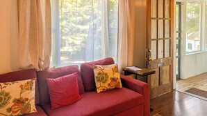 Una sala de estar acogedora con un sofá rojo, cojines estampados y un ventanal con cortinas de encaje.