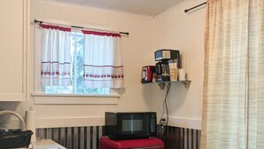 A compact kitchen with a stove, a red refrigerator, a microwave, and a window with curtains.