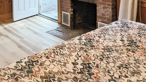 A room with a brick fireplace, a television mounted above it, and a patterned bedspread.