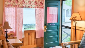 Une pièce chaleureuse avec une porte en bois, une petite table, une chaise, un canapé et un tapis aux couleurs vives.