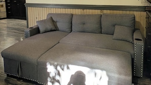 Ein großes Ecksofa mit gepolsterten Kopfstützen und Armlehnen, platziert in einem Raum mit Holzboden und hohen Decken.