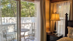 Ein Schlafzimmer mit einem großen Bett, einem Nachttisch, einer Lampe und Blick auf eine Außenpatio mit Stühlen und einem Tisch.