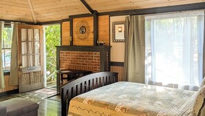 Ein gemütliches Zimmer mit einem großen Bett, einer hölzernen Bank, einem Kamin und Blick ins Freie.