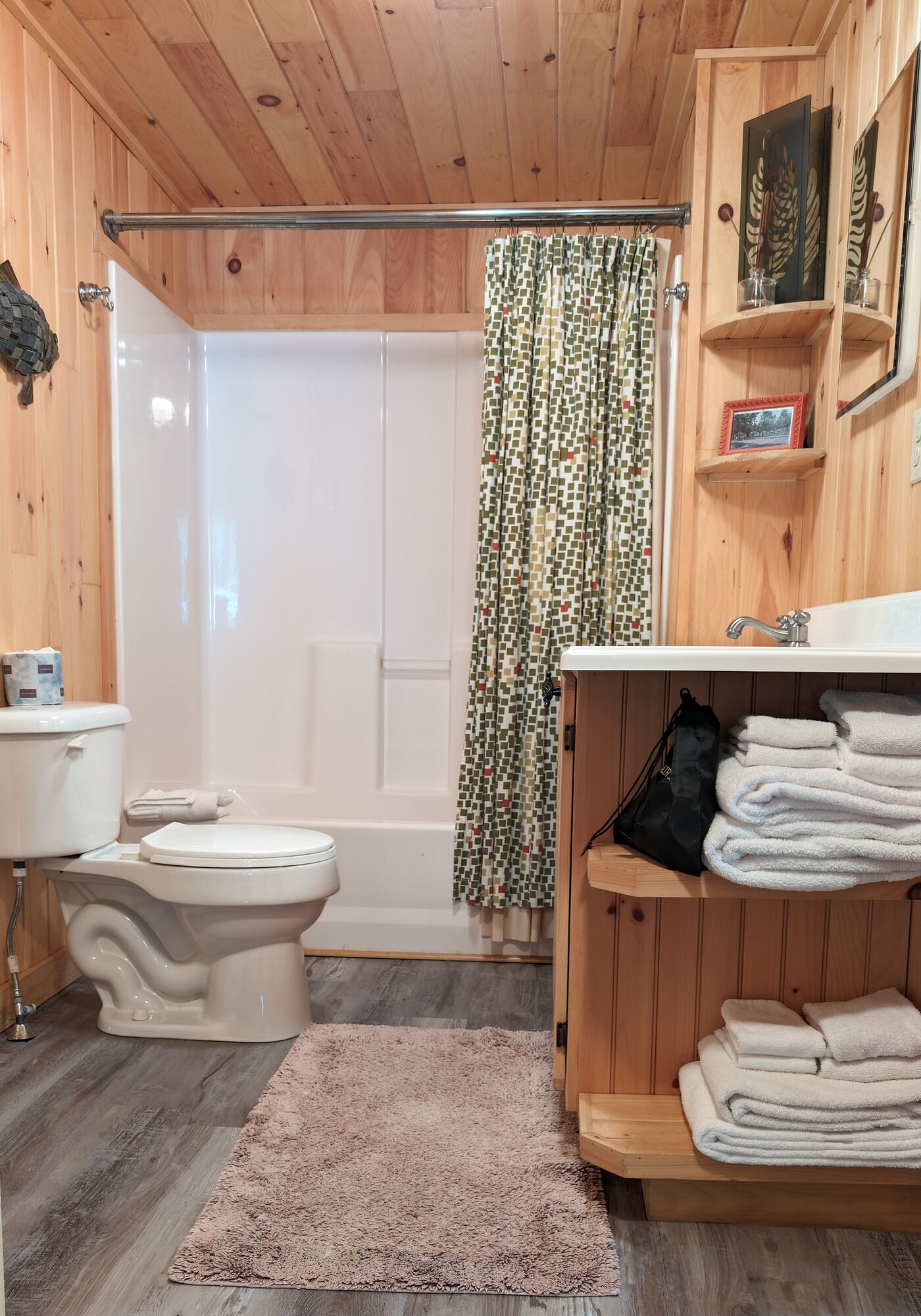 Ein Badezimmer mit Holzwandverkleidung, das eine Toilette, eine Dusche und Holzregale mit Handtüchern bietet.