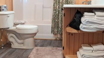 Ein Badezimmer mit Holzwandverkleidung, das eine Toilette, eine Dusche und Holzregale mit Handtüchern bietet.
