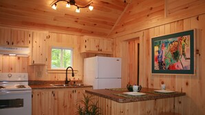 Eine Holzhütte mit einer Küche, inklusive Herd, Spüle, Kühlschrank und Barhocker.