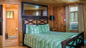 Ein Schlafzimmer einer Holzhütte mit einem Bett, einem Nachttisch, einer Lampe und einem Fenster mit Vorhängen.