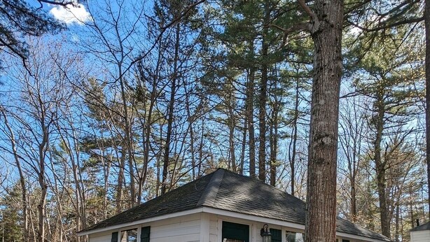 A small cabin with a porch, a green door, and a number '14' on the wall. - Cabin surrounded by Lustrous Pine trees_Cabin 14 (Bar Harbor)