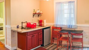A compact kitchen with a sink, a coffee maker, and a small refrigerator. There is a window with sheer curtains and a wooden floor. - Cabin_Wilderness_Acadia_Cabin 15 (Bar Harbor)
