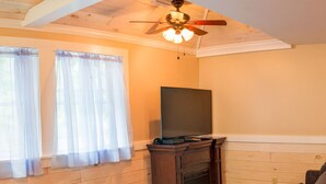 A cozy room with wooden walls, a ceiling fan, a flat-screen TV, and a gray sofa. - Cabin_Wilderness_Acadia_Cabin 15 (Bar Harbor)