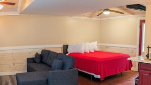 A bedroom with a bed, a gray sofa, a wooden floor, and a ceiling fan. - Cabin_Wilderness_Acadia_Cabin 15 (Bar Harbor)
