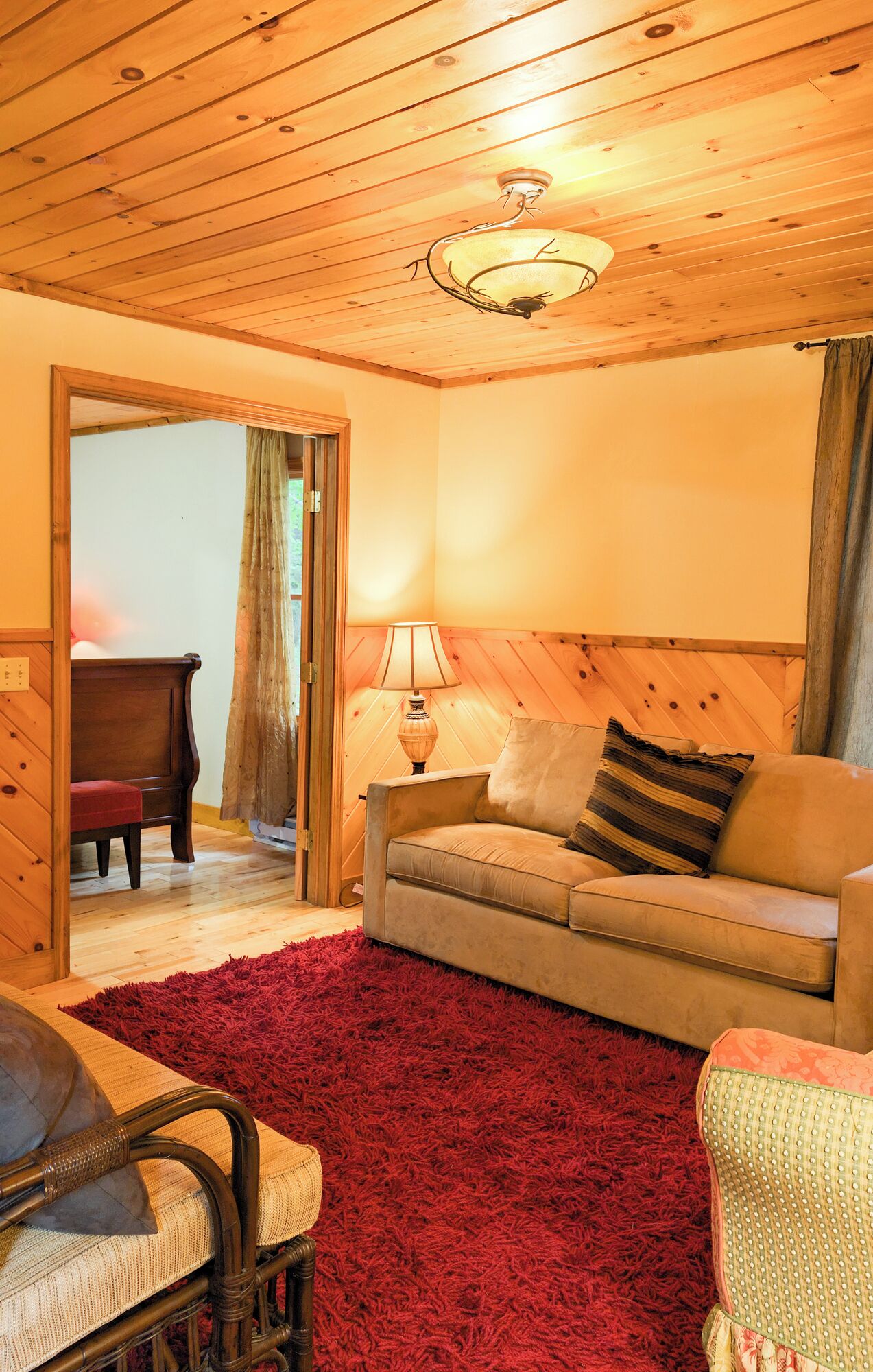 Una habitación acogedora con techo de madera, alfombra mullida roja, un sofá, una lámpara y una silla.