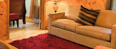 Une pièce chaleureuse avec un plafond en bois, un tapis rouge à longues mèches, un canapé, une lampe et un fauteuil.