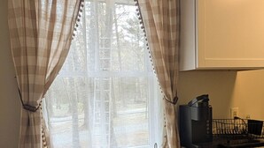 Une cuisine avec une table en bois, une machine à café et une fenêtre avec des rideaux.