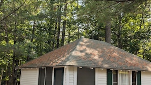 Une petite cabane à un seul étage, dotée d’un toit en pente et entourée de grands arbres.
