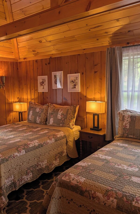 Una habitación acogedora de estilo cabaña, con dos camas, paredes de madera e impresiones botánicas enmarcadas.