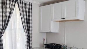 A compact kitchen with white cabinets, a granite countertop, and a black stove. - New Cabin to ENJOY!_Cabin 20 (Bar Harbor)