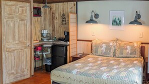 A bedroom with a large bed, wooden ceiling, a kitchen area with a microwave, and a small refrigerator.