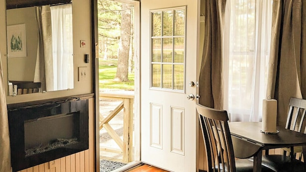 A wooden interior with a dining table and chairs, a fireplace, and a door leading to an outdoor area.