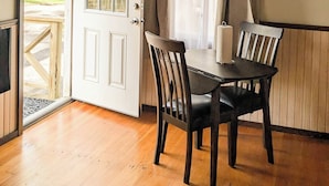 A wooden dining room with a table and chairs, a door leading outside, and a window with curtains.