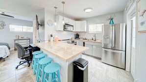 Una cocina moderna con una isla central, taburetes de bar, electrodomésticos de acero inoxidable y vistas al dormitorio contiguo.