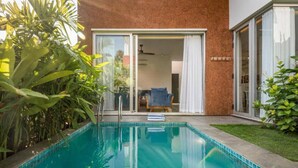 Una piscina con un recinto in vetro, una zona patio con una sedia e un'ampia vetrata che dà su un ambiente interno.