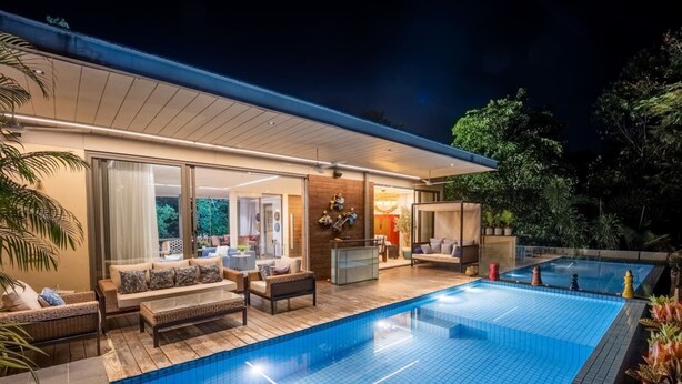A modern outdoor pool area with a wooden deck, lounge seating, and a glass-enclosed living space. - Avior by Hireavilla - 4BR w Infinity Pool in Parra (Parra)