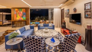 A modern living room with a blue sofa set, a round coffee table, and a TV mounted on the wall. - Avior by Hireavilla - 4BR w Infinity Pool in Parra (Parra)