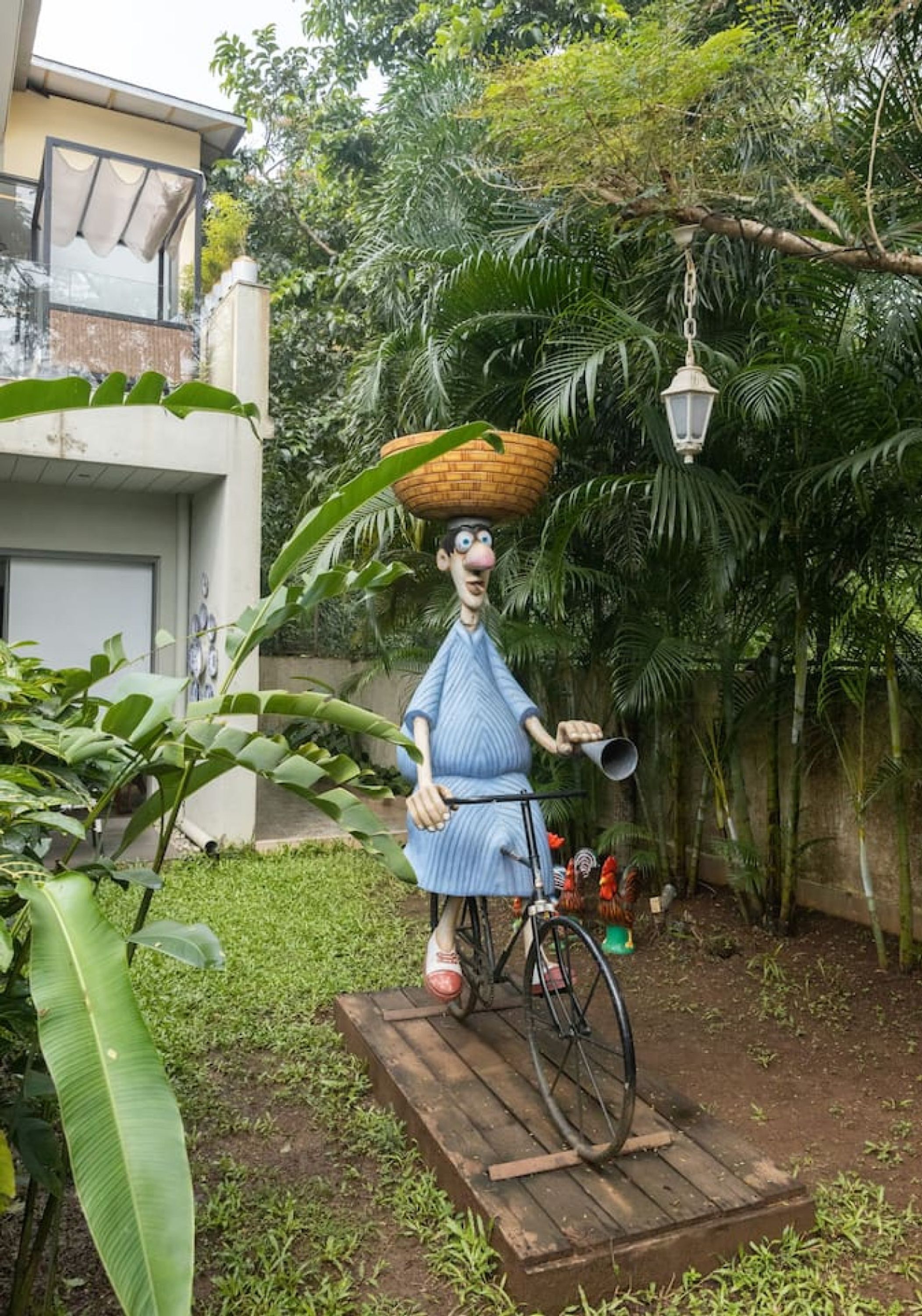 Una estatua de una figura con una cesta en la cabeza, sobre una plataforma de madera junto a una bicicleta.