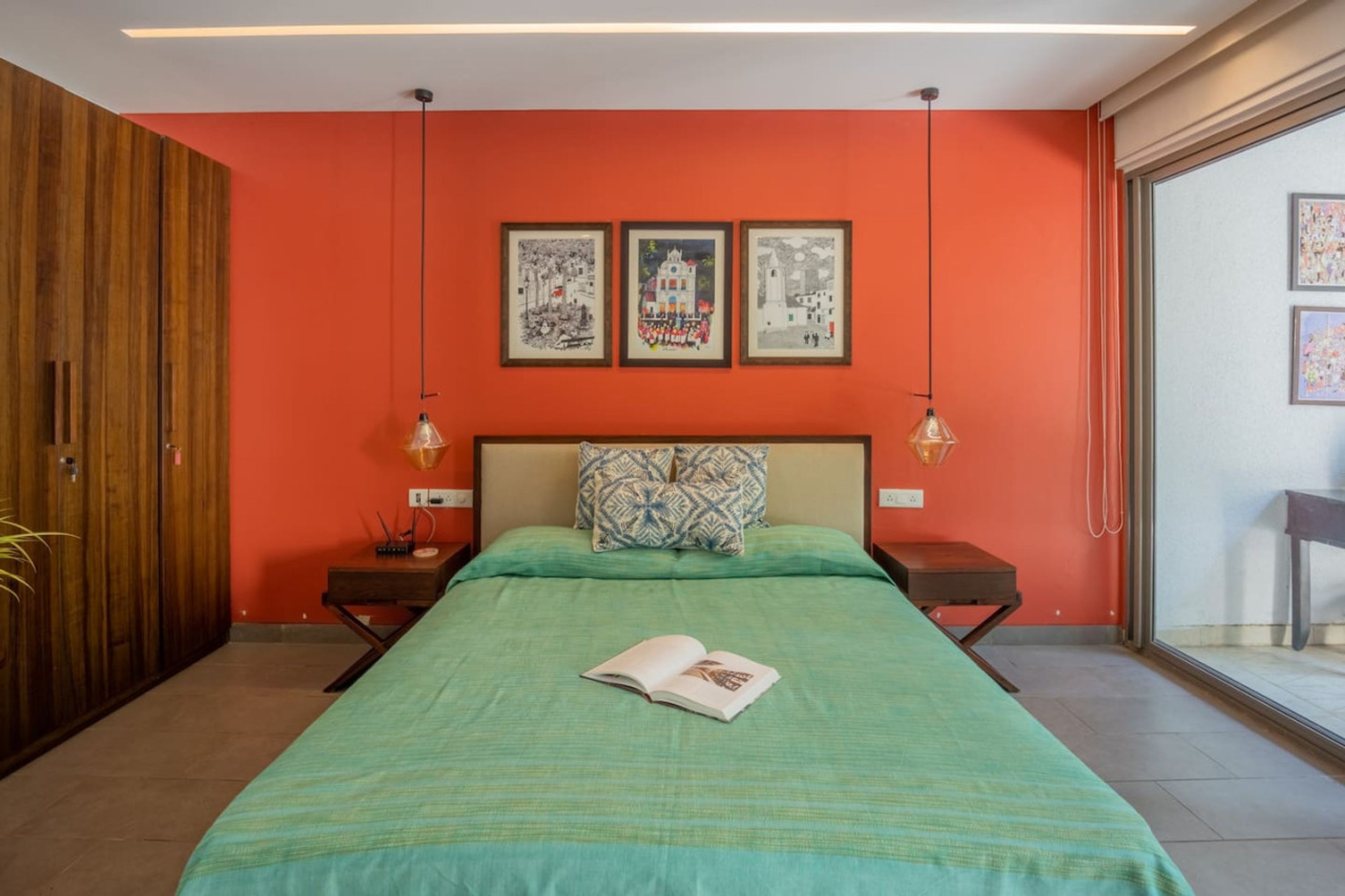 A bedroom with a green bedspread, a wooden wardrobe, and a large window with a view.