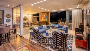 A modern living room with a blue sofa set, patterned chairs, a coffee table, and a large painting on the wall. - Avior by Hireavilla - 4BR w Infinity Pool in Parra (Parra)