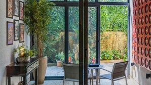 A room with a large glass door leading to a garden, a potted plant, a small table, and chairs. - Avior by Hireavilla - 4BR w Infinity Pool in Parra (Parra)