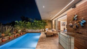 Un área de piscina moderna al aire libre con un deck de madera, sillas de descanso y una pared decorada con instrumentos musicales.