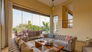 A spacious living room with a large window, a sofa set, a coffee table, and a view of the outdoors. - Cliffhouse by Hireavilla -5br w Pvt Pool in Saipem (Candolim)