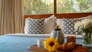 A bed with patterned pillows, a wooden headboard, and a view of greenery outside. - Cliffhouse by Hireavilla -5br w Pvt Pool in Saipem (Candolim)