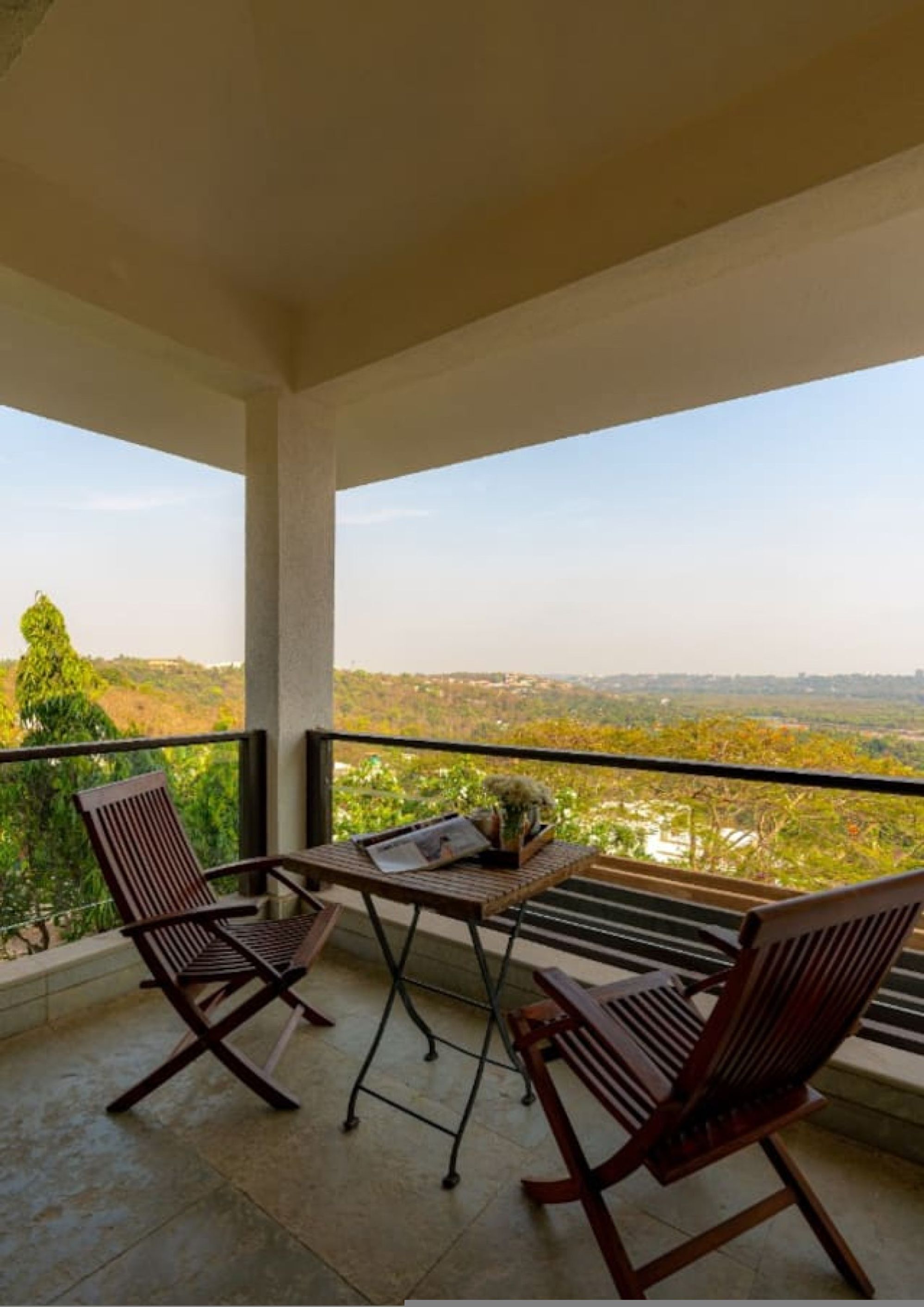 A balcony with two wooden chairs and a small table, overlooking a lush landscape.